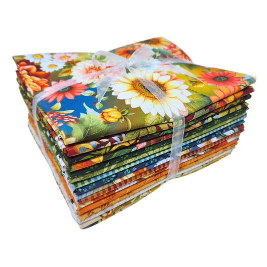 A stack of colorful fabric bundles tied together with a sheer white ribbon, featuring a vibrant floral and botanical print with sunflowers, daisies, and green leaves.