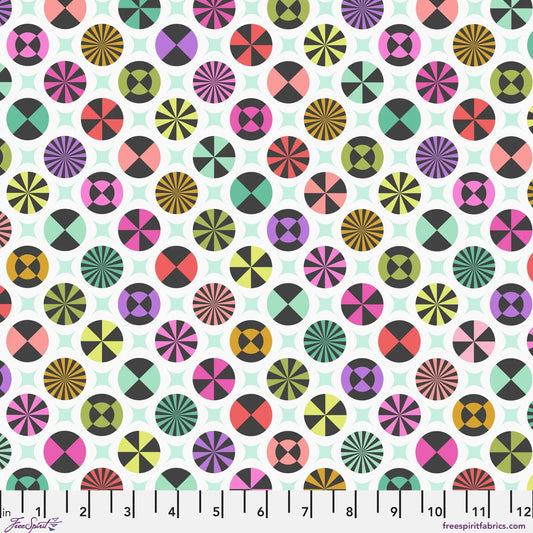 A repeating fabric pattern featuring colorful geometric medallions and pale mint-green star shapes on a white background, with a ruler along the bottom edge showing scale.