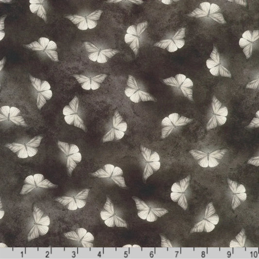 Patterned fabric of softly glowing white moth silhouettes scattered across a dark, mottled charcoal grey background with a ruler at the bottom for scale.