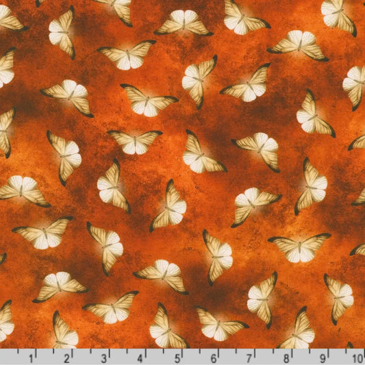 Patterned fabric of softly glowing white moth silhouettes scattered across a mottled burnt-orange background with a ruler at the bottom for scale.