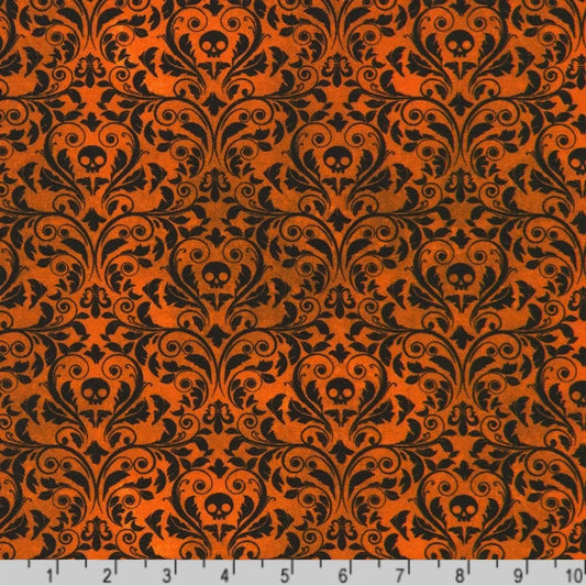 An ornate black damask pattern with small skull motifs on a warm, burnt-orange background with a ruler at the bottom for scale.
