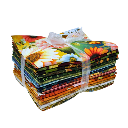 A stack of colorful fabric bundles tied together with a sheer white ribbon, featuring a vibrant floral and botanical print with sunflowers, daisies, and green leaves.