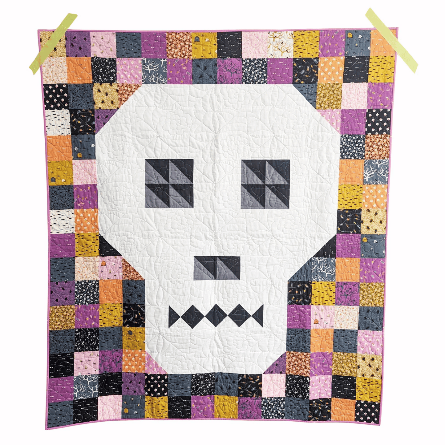 The Bonedigger Quilt features a white pieced skull surrounded by patchwork squares of various Halloween fabrics. 