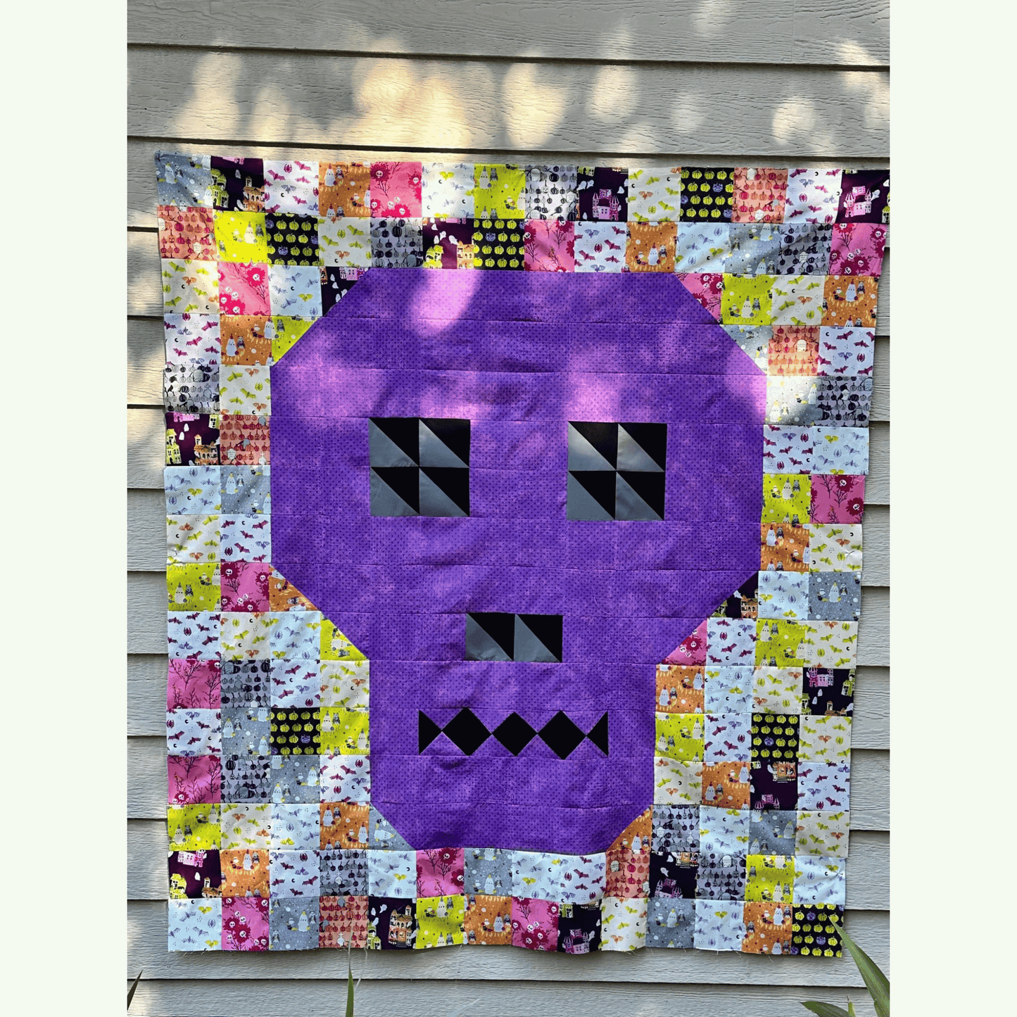 The Bonedigger Quilt features a purple pieced skull surrounded by patchwork squares of various Halloween fabrics. 