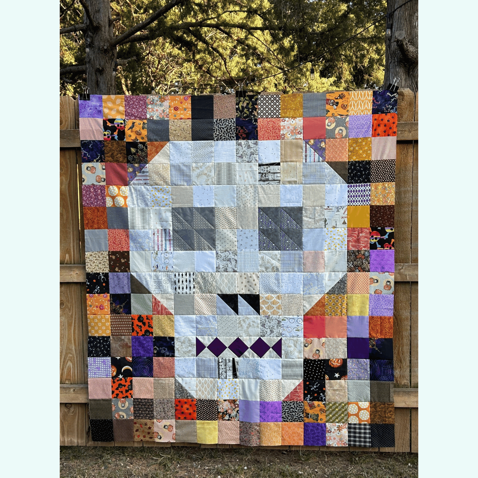 The Bonedigger Quilt features a white and grey pieced skull surrounded by patchwork squares of various Halloween scrappy fabrics. 