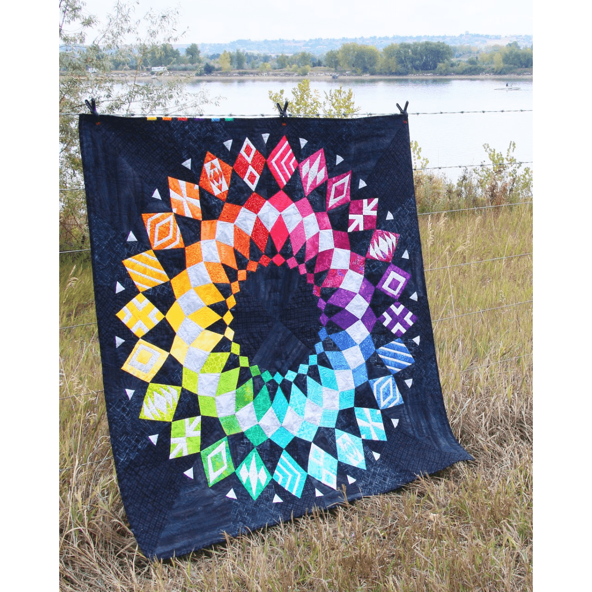 The Cadence Court Quilt made with wedges in a rainbow gradient against a dark blue/black background.