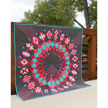 The Cadence Court Quilt made with pink, red, and aqua blue wedges against a dark red and black background.