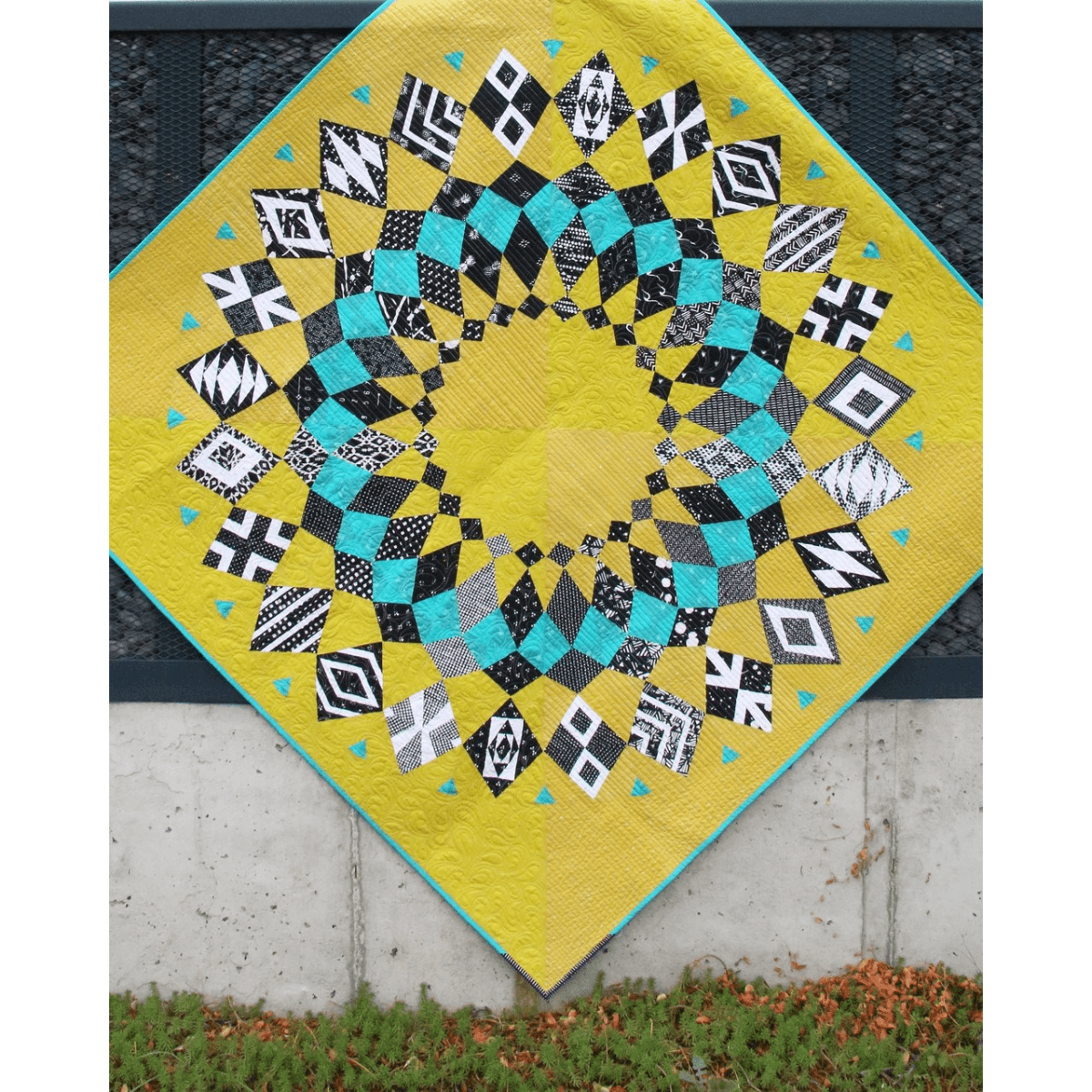 The Cadence Court Quilt made with black, white, and aqua blue wedges against a bright lime green background.