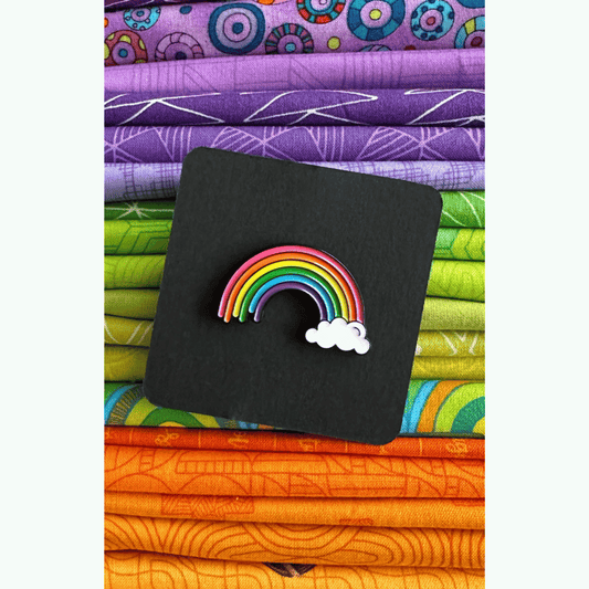 The Happy Highway Rainbow Enamel Pin features a curvy doodle of a rainbow sitting on a cloud on one side.