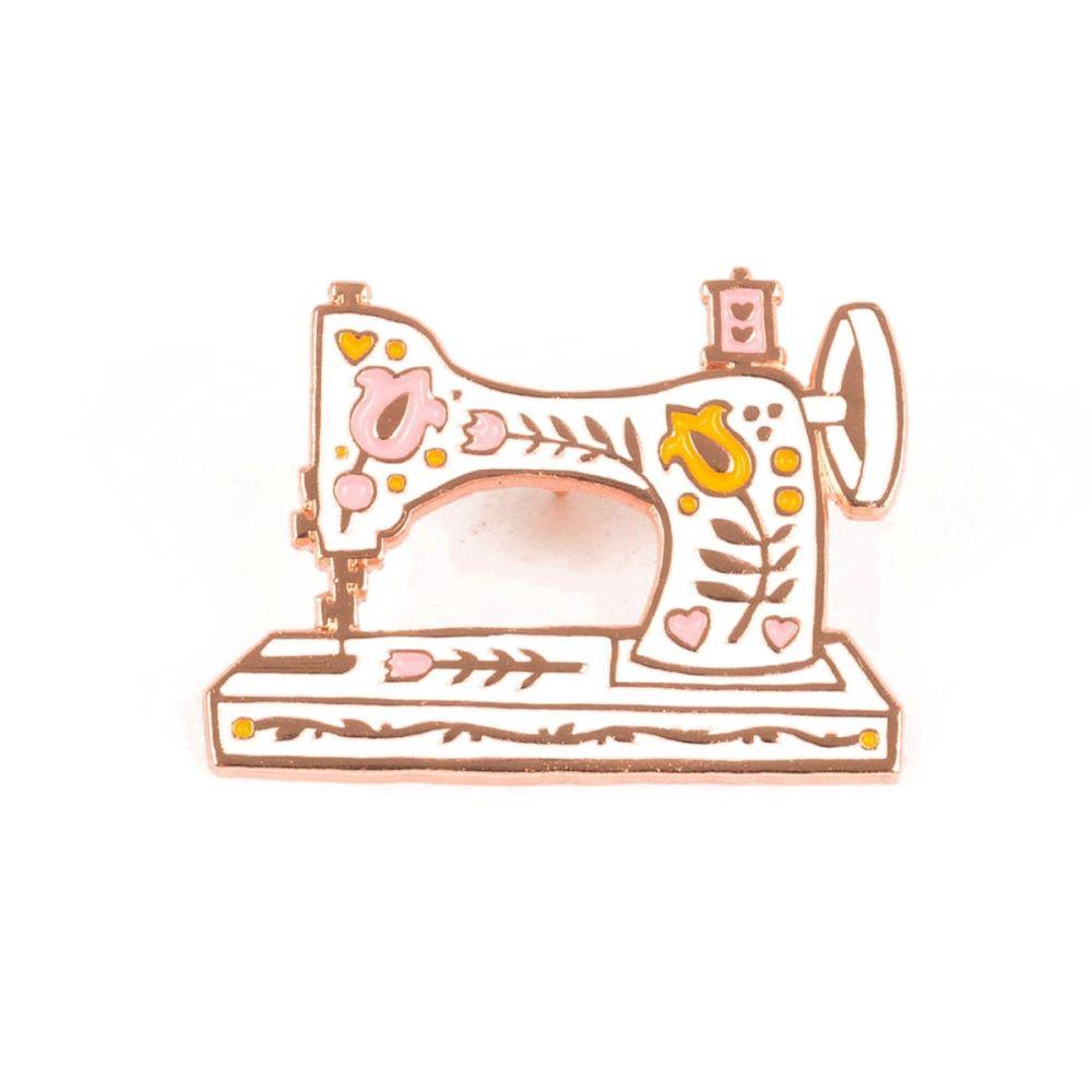 This Vintage White Sewing Machine Enamel Pin from Maker Valley features a hand-drawn vintage sewing machine in white, orange, and pink with sparkling metallic rose gold trim.