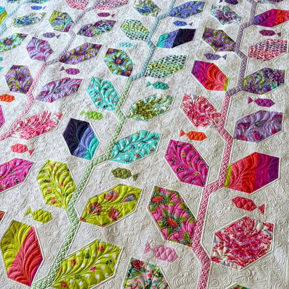 A close-up detail of the Marine Meadows finished quilt featuring elongated hexagon and diamond-shaped fabric pieces in vibrant pinks, purples, teals, and chartreuse prints, set against a cream white background with dense swirling free-motion quilting.