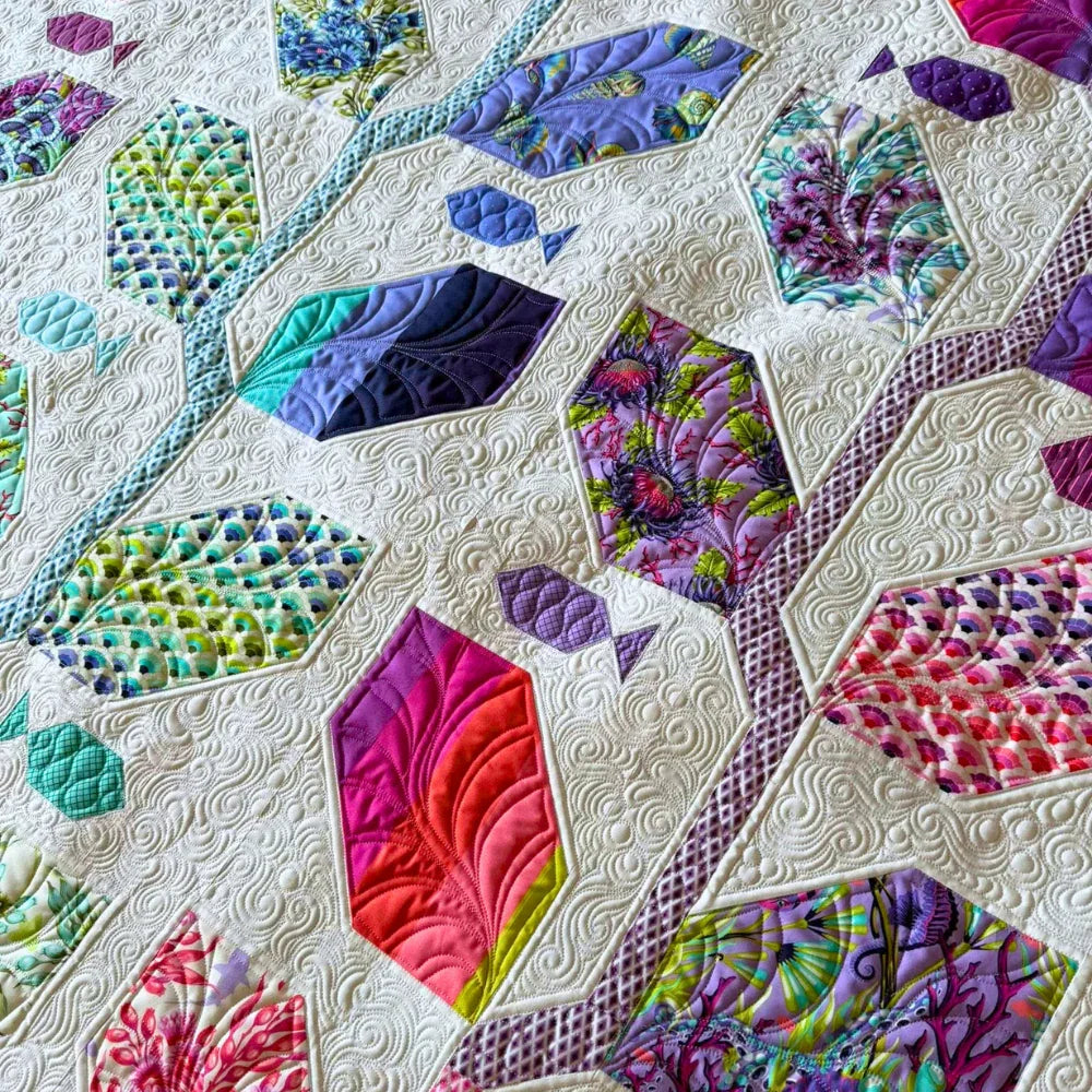 A close-up detail of the Marine Meadows finished quilt featuring hexagonal leaf blocks in purples, magenta, teal, and chartreuse prints set against a cream white background with dense swirling free-motion quilting.