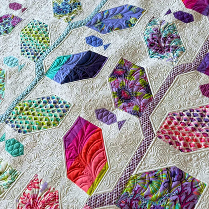 A close-up detail of the Marine Meadows finished quilt featuring hexagonal leaf blocks in purples, magenta, teal, and chartreuse prints set against a cream white background with dense swirling free-motion quilting.