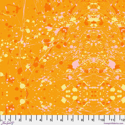 Abstract paint-splatter fabric pattern in bright orange, with scattered pink and yellow splashes and drips. Ruler at the bottom for scale.
