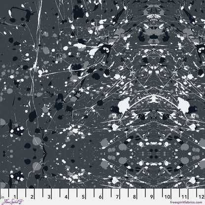 Abstract paint-splatter fabric pattern in charcoal grey, with scattered black and white splashes and drips. Ruler at the bottom for scale.