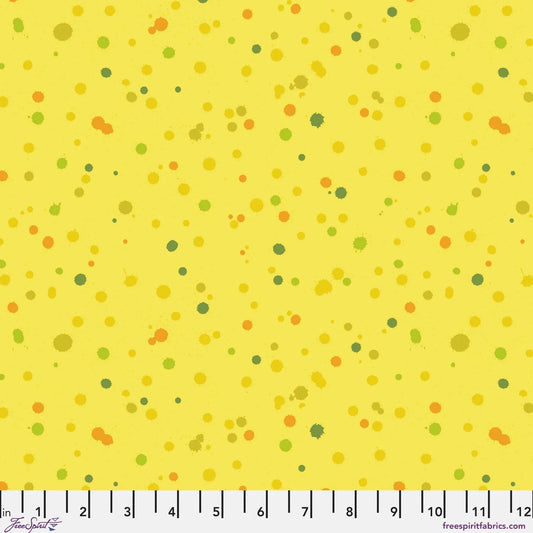Fabric design of paint droplets in olive, orange, and chartreuse tones scattered across a warm, sunny yellow background. Ruler at the bottom for scale.