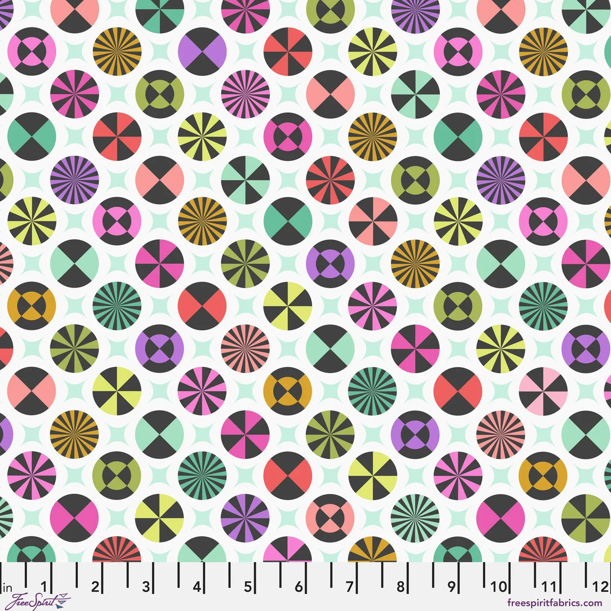 A repeating fabric pattern featuring colorful geometric medallions and pale mint-green star shapes on a white background, with a ruler along the bottom edge showing scale. 