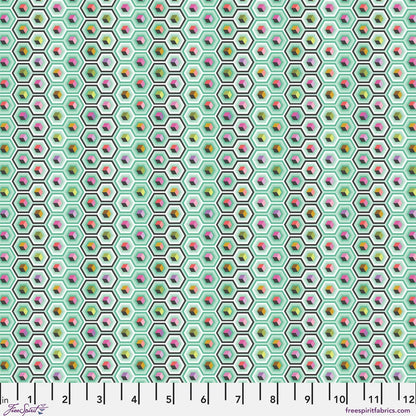 A repeating geometric fabric pattern of small hexagons on a mint green background, each containing colorful cube motifs in pink, yellow, orange, green, and purple. Ruler at the bottom for scale.