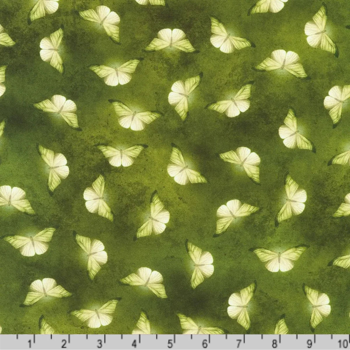 Patterned fabric of softly glowing white moth silhouettes scattered across a mottled olive and chartreuse-green background with a ruler at the bottom for scale.