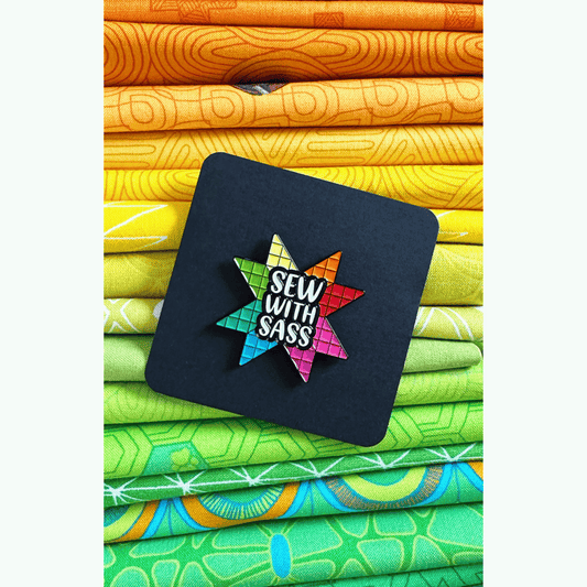 The Sew With Sass Enamel Pin features the phrase "Sew With Sass" situated in the center of a colorful pieced Carpenter’s Star block!