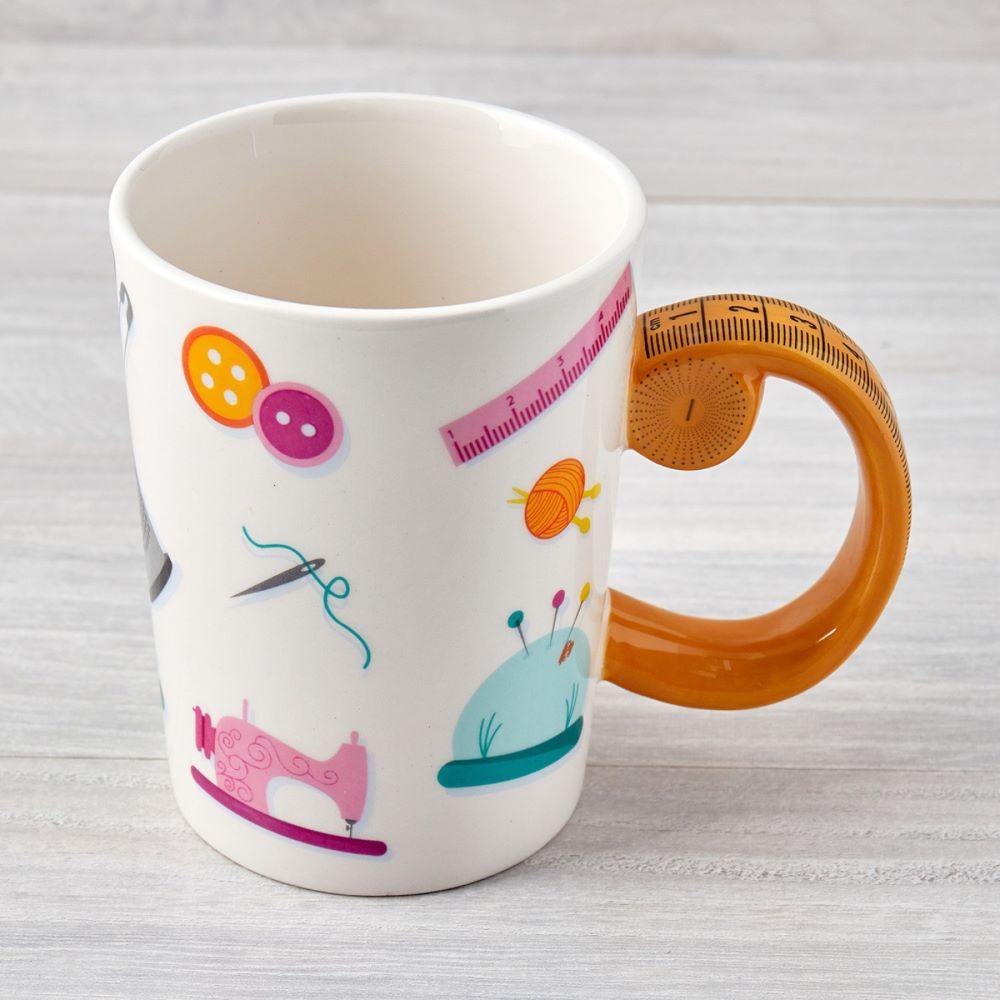 The Tape Measure Sewing Mug features assorted notions like rulers, buttons, needles, pincushions, and sewing machines printed on the sides, and the handle looks like a partially rolled measuring tape.