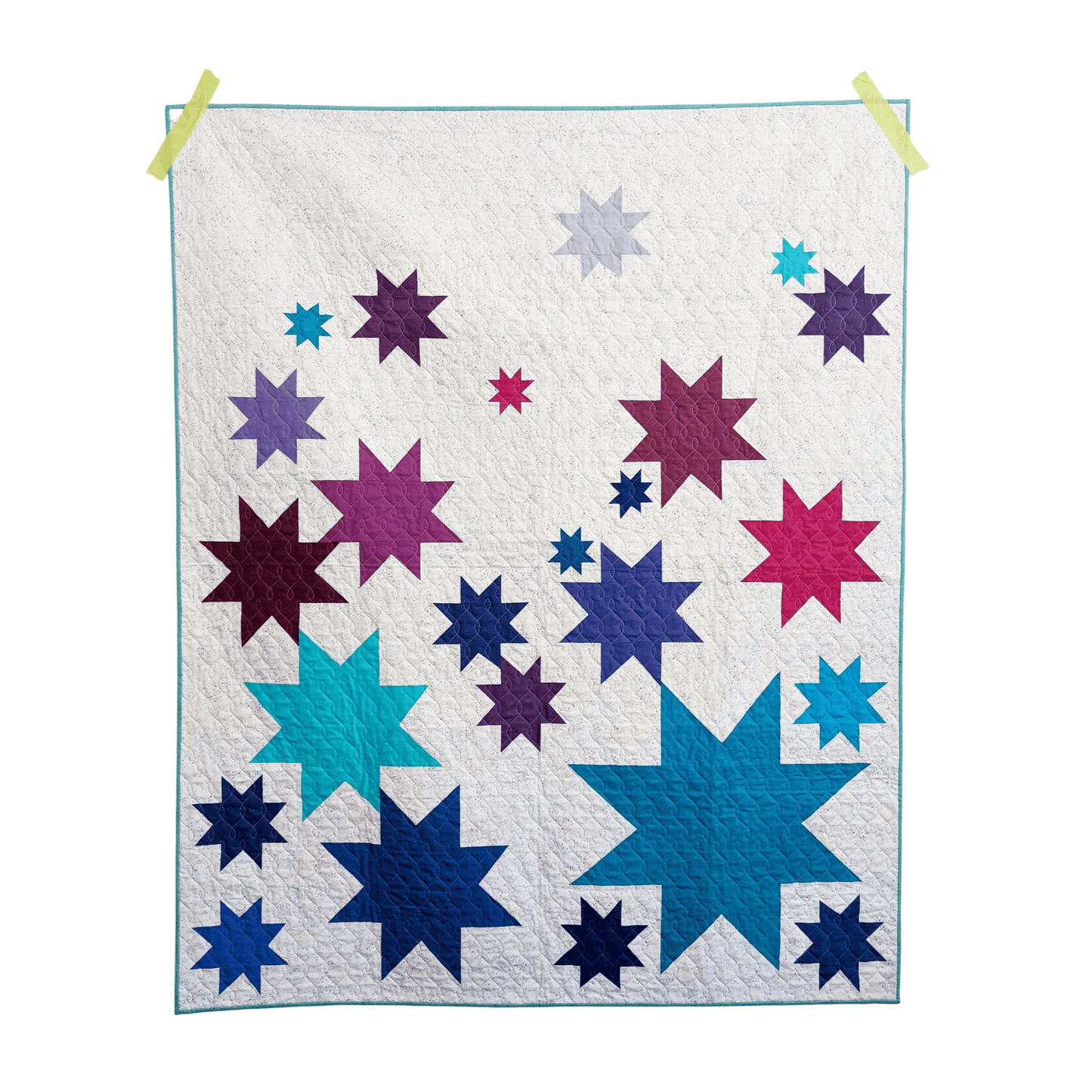 The Vela Quilt is a fun take on wonky stars. This modern quilt features various sized star blocks in blue, pink, and purple pieced with a white background fabric.