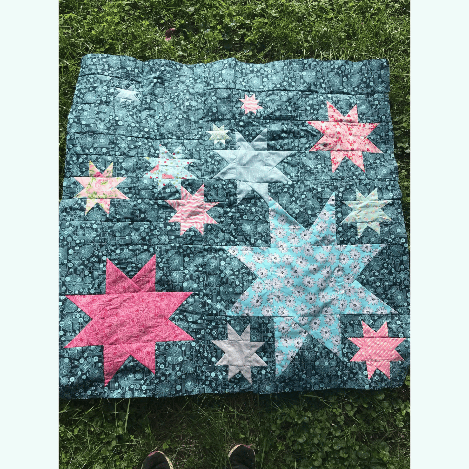 The Vela Quilt is a fun take on wonky stars. This modern quilt features various sized star blocks in blue and pink pieced with a blue floral background fabric.